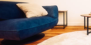 Blaues Sofa mit einem beigen Kissen, Holzboden, zwei Beistelltische und ein runder Teppich.