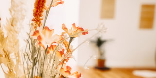 Ein Blumenstrau&szlig; mit orangefarbenen und wei&szlig;en Bl&uuml;ten im Vordergrund, unscharfer Hintergrund mit Holzboden und Wanddekorationen.
