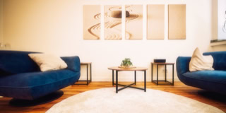 Ein Wohnzimmer mit zwei blauen Sofas, einem runden Teppich, einem kleinen Tisch mit Pflanze und vier Wandbildern.